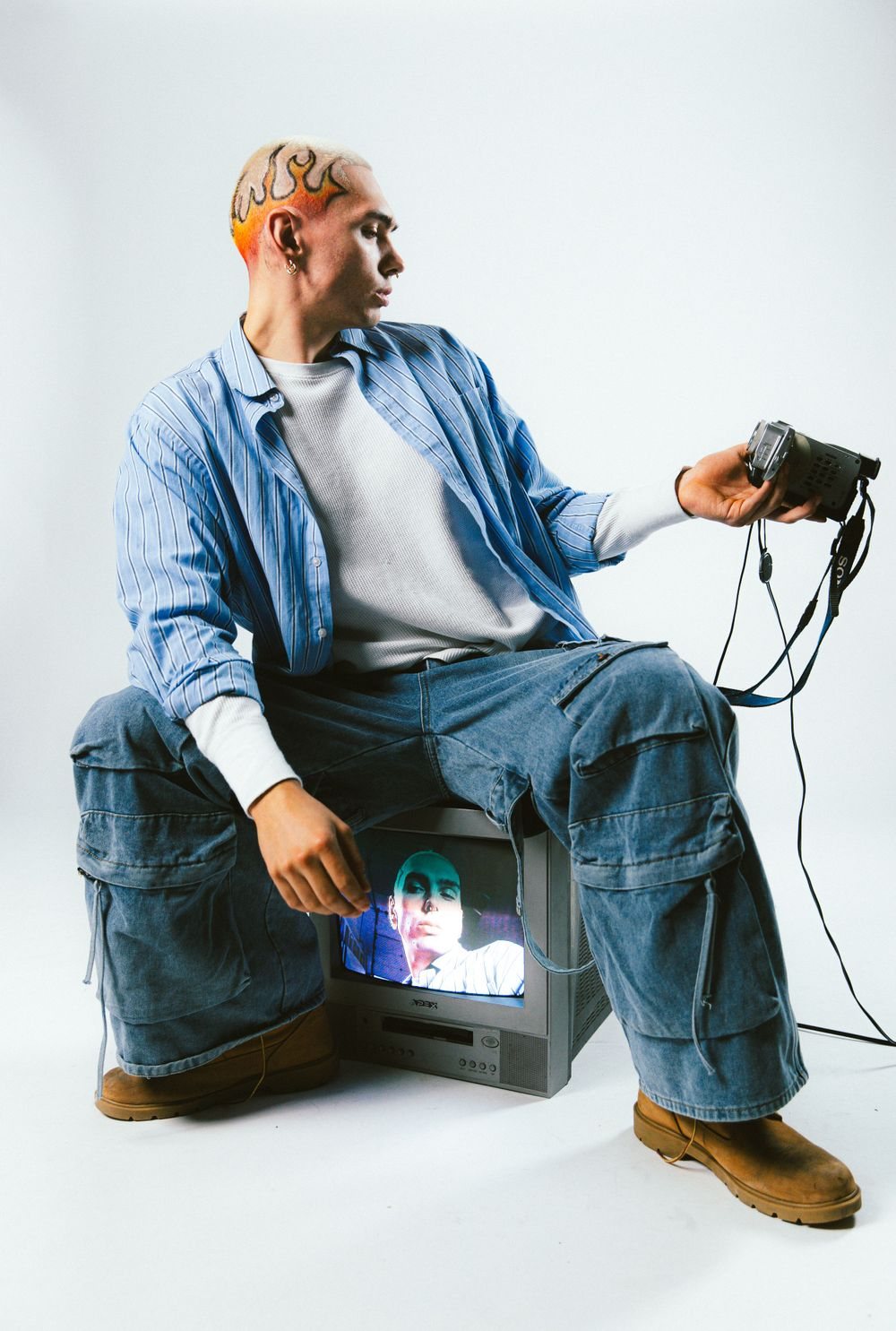 Man in denim seated on an old TV holding a camera